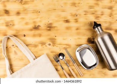 Stainless Steel Tableware; Spoon, Fork, Chopsticks, Lunch Box And Drinking Water Bottle Lay On Wooden Table With Eco Friendly Tote Bag Cut Off. Flat Lay With Copy Space.