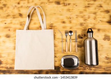 Stainless Steel Tableware; Straw, Spoon, Fork, Chopsticks, Lunch Box And Reusable Bottle Lay On Wooden Table As A Background With Eco Friendly Tote Bag.