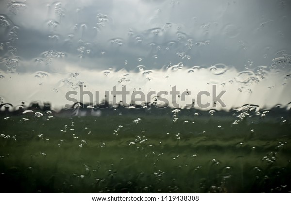 Stains of rain on windscreen. Green field and dark\
stormy sky behind the\
glass.