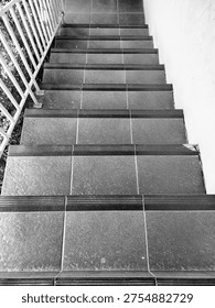 A staircase consisting of dark gray steps with black wavy strips at the ends for anti-slip protection. On the left side of the staircase is a cream or light yellow guardrail with vertical bars.