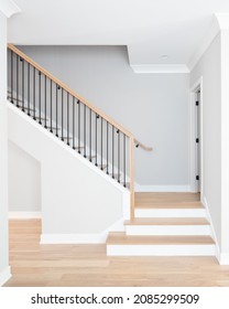 A staircase going up with natural wood steps and handrails, white risers, and wrought iron spindles. - Shutterstock ID 2085299509