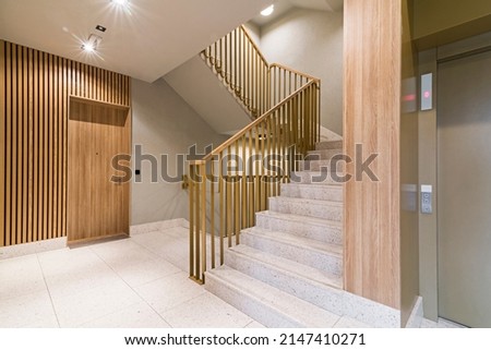 Staircase in modern block of flats. Finished with wood wall panels, tile floor. Interesting balustrade.