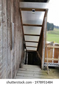 A staircase on the side of a wooden farmhouse down to the carport.