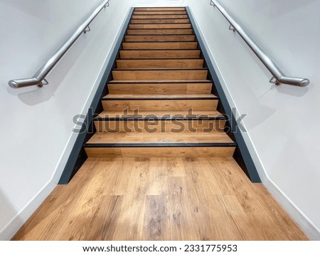 The staircase steps are made of brown wood and have stainless steel handrails on both sides.