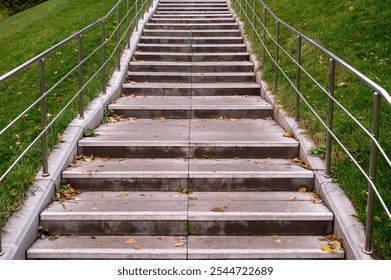 Staircase with stone steps and steel railings. Hill with green grass. Staircase in the park covered with autumn leaves. - Powered by Shutterstock