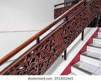 A staircase with white tiles and a wooden railing. The railing is intricately carved with floral patterns and has a dark brown color. The background is a white wall - Powered by Shutterstock