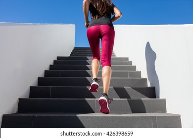 Stairs climbing running woman doing run up steps on staircase. Female runner athlete going up stairs in urban city doing cardio sport workout run outside during summer. Activewear leggings and shoes.