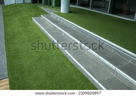 Stairs at the entrance of building with artificial turf or synthetic grass covered the floor. Concept of presentable fake grass installed on the ground, landscaping project or residential lawn