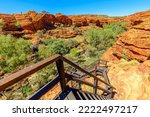 Stairs at Kings Canyon leading down to Garden of Eden, Watarrka National Park, Northern Territory. Aerial rugged landscape, red sandstone, gum trees at canyon gorge. Outback Red Center, Australia.