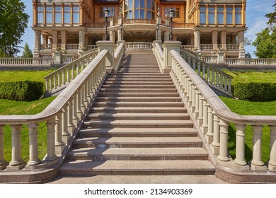 Stairs with stone railings balusters and iron lanterns on the background of the park with a luxurious landscape design walking path for walking, green lawns and a variety of bushes.