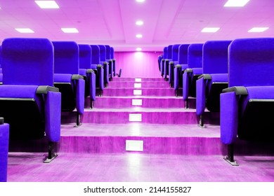 stairscase gallery between empty rows of seats of an auditorium with violet reclining rows of seats and false ceiling led lights