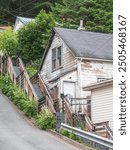 Stairway with intermediate landings between the front of a weathered house and the edge of a hilly street in a residential neighborhood in Juneau, Alaska, on an overcast morning late in spring