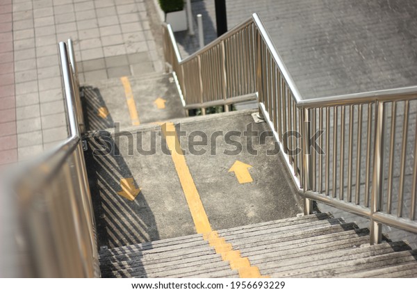 Stairway to the old, grungy stair footbridge or\
overpass with  yellow line divided into two sides for walking up\
and down, Stainless steel railing for people walk cross the road\
crossing safety.