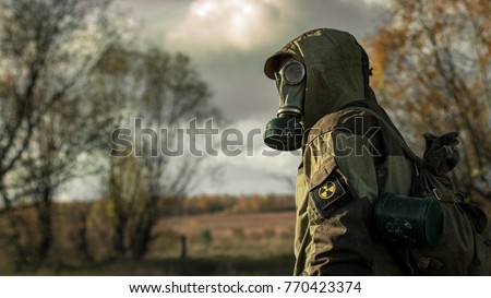 Stalker soldier in gas mask and russian military hoodie jacket looking backwards while walking in the danger radioactive zone. Post apocalypse. Nuclear war.