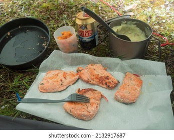 Staloluokta, Sweden, Agust 12, 2021: Fried Trout Fish Fillet, Arctic Char With Mashed Potatoes In Cooking Pan And Mess Tin, Ripe Cloudberries And Norrlands Guld Beer Can. Outdoor Camping Dinner