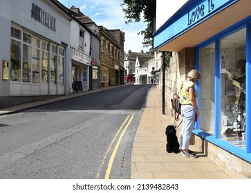Stamford, Lincolnshire, UK - Jun 01, 2019:  An elegant lady with her adorable dog outside a trendy shopfront window, in the high street of Stamford, a charming medieval city. 