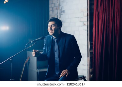 Stand Up Comedian On Stage. Young Man Talks Joke Into Microphone Or Sings Songs.