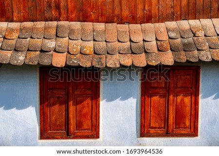 stand in front of a brick house with shutters and a wooden roof