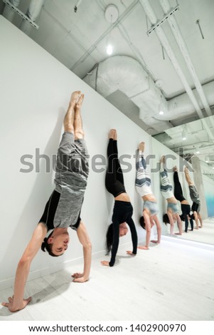 Stand near women. Strong man wearing grey shorts and t-shirt practicing arm stand near women