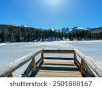 Stand on overlook bridge looking at a frozen lake and the mountains in Rocky Mountain national park 