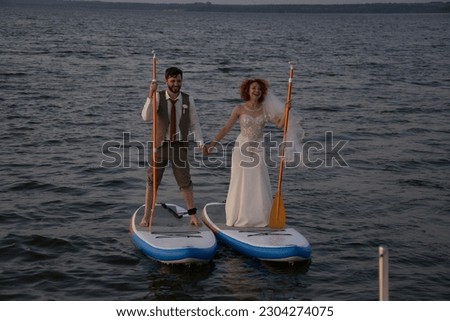 Stand up paddle boarder exercising in the river young man and woman in wedding suits