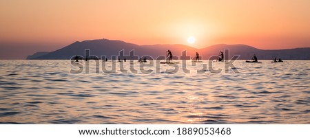 Stand up paddle boarders SUP silhouettes on the water of the sea. Evening, sunset at sea. Active rest on the sea