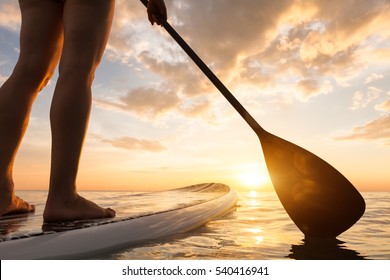Stand up paddle boarding on a quiet sea with warm summer sunset colors, close-up of legs