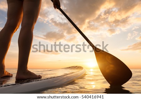 Stand up paddle boarding on a quiet sea with warm summer sunset colors, close-up of legs