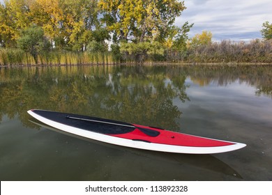 Stand Up Paddleboard With Paddle On A Calm Lake In Fall Scenery