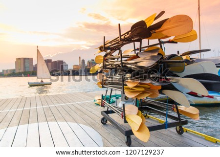 stand with paddles on a wooden pier by the river. sailing boat at sunset. Blurred background, copy space for your text