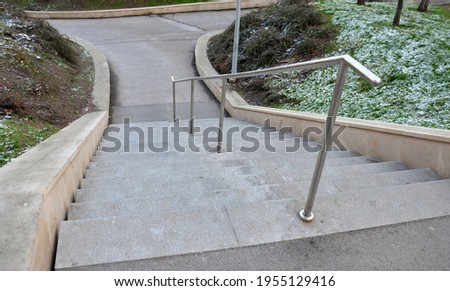 stand in the park made of concrete with a handle made of shiny, stainless steel metal pipes. lower railing is a protection against falling from too long and steep stairs down, it is centrally located