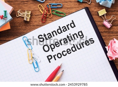 Standard Operating Procedures Manual on Wooden Desk Surrounded by Office Supplies
