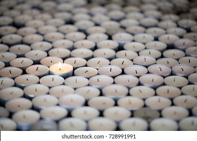 Standing alone. Single resilient flame keeps burning amongst many extinguished tealight candles. Solitary shining light stands out with selective focus.