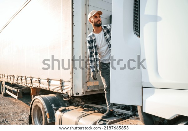 Standing behind the cabin. Young truck driver is\
with his vehicle at\
daytime.