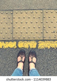 Standing behind the yellow line with sandals