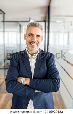 Standing in a bright corridor, a mature businessman presents a portrait of professionalism and accessibility, embodying the dynamism of the modern work environment