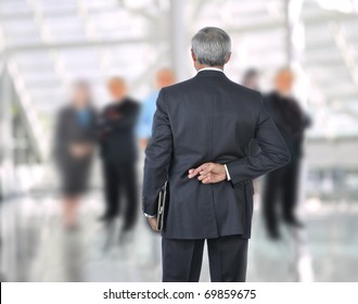 Standing Businessman with fingers crossed behind back. He is standing in front of an out of focus group of people. Horizontal format. - Powered by Shutterstock