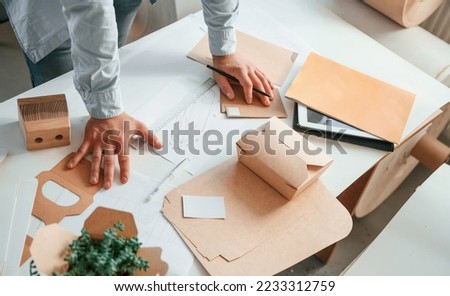 Standing by the table and looking at draws. Print house worker in white clothes is indoors.