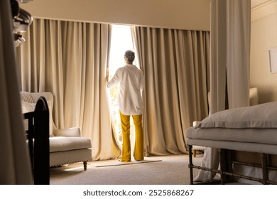 Standing by window, senior woman opening curtains in cozy living room, copy space. Home, domestic, lifestyle, relaxation, morning, sunlight - Powered by Shutterstock