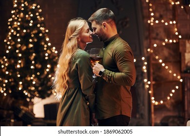 Standing and holding big glasses with wine. Young lovely couple have romantic dinner indoors together.