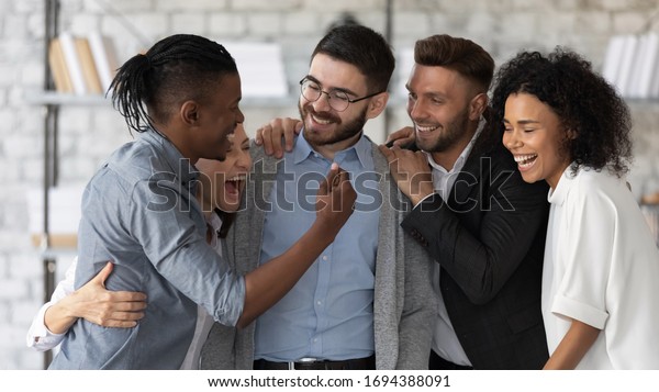 Standing and hugging smiling team laughing\
looking at each other. Happy diverse corporate staff, laughter\
specialists, company representatives, bank workers photo shoot, HR\
agency recruitments.