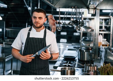 Standing and looking at the camera. Chef is on the kitchen preparing food.