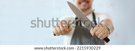 Standing man holding in hand sharp kitchenware for cooking, knife sharpening process