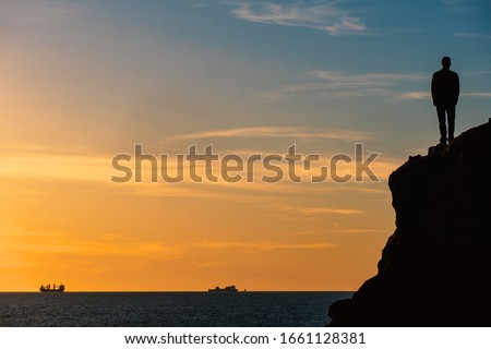 Standing man silouette on a rock in front of the sea at sunset. Conceptual image for future projects with copy space.