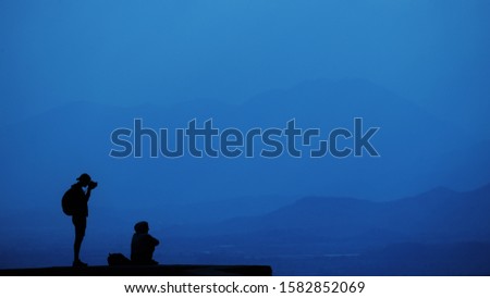 Standing man and sitting woman relaxing on top of a mountain and enjoying a valley. Beautiful sky view panorama. Travel lifestyle hiking concept vacations outdoor. Classic blue 2020 year color concept