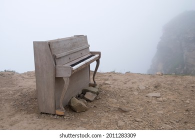 standing on the edge of the cliff, fog is visible on the rocks, and on the edge of the cliff there is an old piano, green grass is breaking through the stones, the day is cloudy and foggy