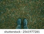 Standing on lush green grass meadow ground, feet with boots from above, top view