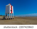 Standing on stilts, the wooden lighthouse on the beach near Burnham on Sea. The lighthouse is painted white with a single vertical red stripe on its front.