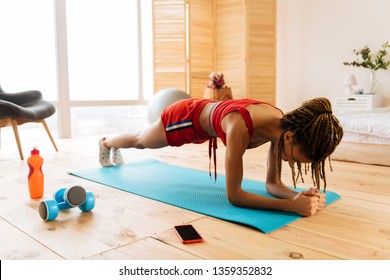 Standing in plank. Woman with nice braids wearing red shorts and top standing in plank at home - Powered by Shutterstock