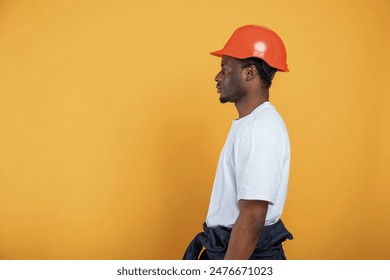 Standing and posing, construction worker in hard hat. Handsome black man is in the studio against yellow background. - Powered by Shutterstock